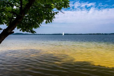 A beautiful lagoon with clear water. A lonely sailboat in the background. Sunny day. Holidays. Lake Dzieckowice, Poland