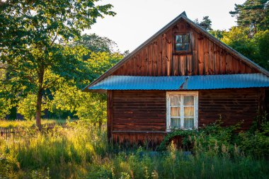 Beautiful rural landscape. Old wooden cottage with a white window. Afternoon sun