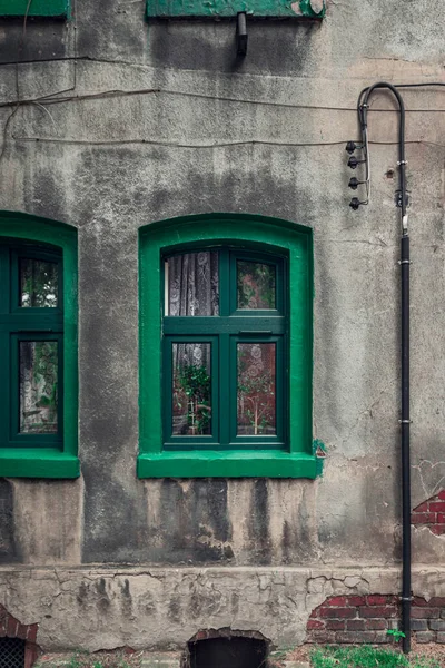 A green window with a green window sill against the background of a gray, plastered, damaged wall