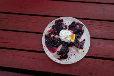 Peynirli hamur tatlısı, yaban mersini soslu krema ve beyaz tabakta servis edilen portakal garnitürü.