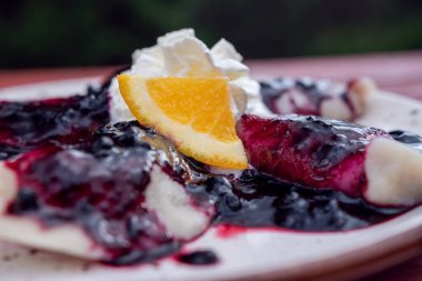 Peynirli hamur tatlısı, yaban mersini soslu krema ve beyaz tabakta servis edilen portakal garnitürü.