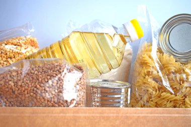 Karton bir kutuda çeşitli konserve yiyecekler, makarna ve mısır gevrekleri. Yiyecek bağışları ya da yiyecek teslimatı kavramı.