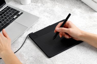 Eller masada otururken grafik tablet ve dizüstü bilgisayar kullanıyor. Proje üzerinde çalışıyorum. Mesafeli iş. Tasarımcı veya fotoğrafçı