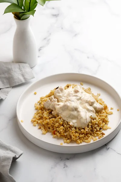 Tavuk ve krema soslu bulgur. Bulgur lapası ve tavuk filetosu ile akşam yemeği fikri. Beyaz arkaplan ve beyaz plaka