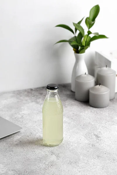 Masada dizüstü bilgisayarla bir şişe limonata. Mumlar ve arka planda vazo. Model