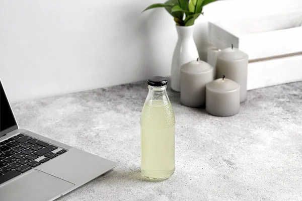 Masada dizüstü bilgisayarla bir şişe limonata. Mumlar ve arka planda vazo. Model