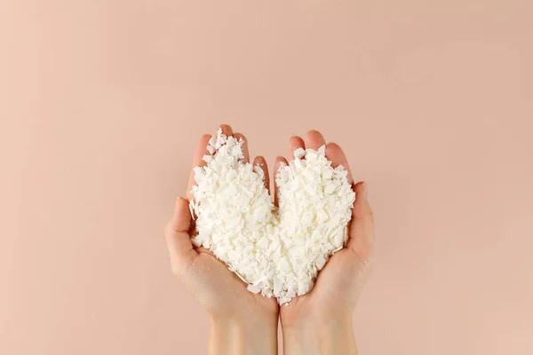 Hand with organic white Soy wax flakes for candles and sachet. Heart. Flatlay, top view. Natural soy and coconut wax for candlemaker.