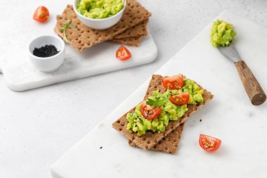 Ekmeğe avokado ezmeli sandviç, domatesli kiraz ve beyaz masada roka. Kahvaltı.