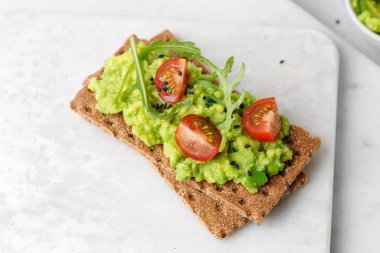 Avokado dilimleri, domatesler ve siyah susam tohumlu sağlıklı kahvaltı ekmeği..