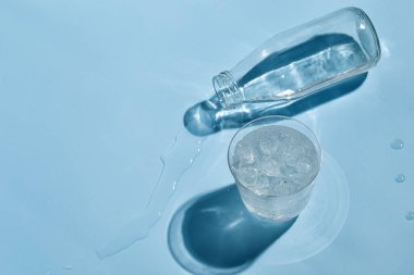 Yalancı su şişesi. Bir bardak su. Güneşli mavi arka planda buzlu. Karanlık gölge