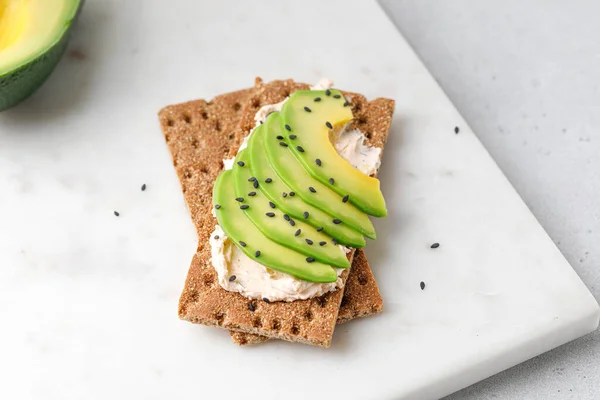 Kepekli tost ekmeğinde avokado, mermer beyaz tahtanın üzerinde susam tohumları.