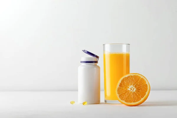 Bardakta taze portakal suyu ve beyaz masada bir şişe vitamin. Vitamin eksikliği