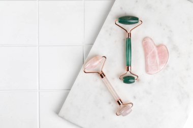 Doğal nefrit taşı silindiri ve Rose kuvars silindirli masaj aleti ve guache kazıyıcı. Mermer tahtada kaplıca cilt bakım ekipmanı.