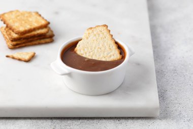 Beyaz sos kabında mermer arka planda çikolata ezmeli kraker ya da kurabiyeler.