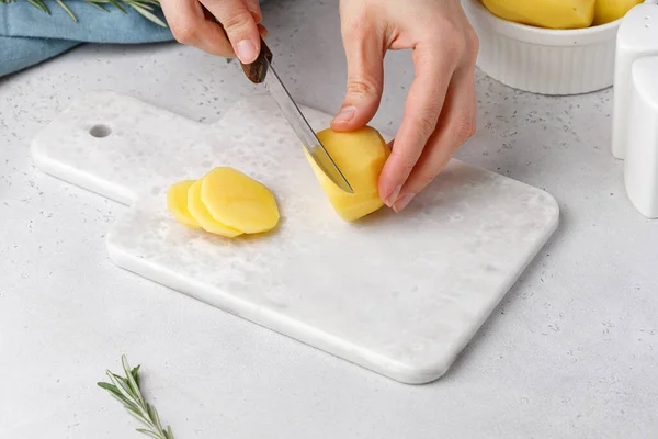Adım adım patates graten tarifi. Eller mermer tahtada patates kesiyor. Patates güveci.