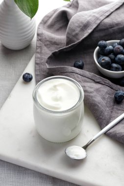 Boş Yunan beyazı yoğurt cam kavanozda mermer tahtada kaşık, vazo, gri peçete ve yaban mersini ile.
