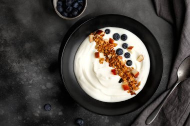 Greek yogurt with Granola with coconut, apple pieces in bowl. Breakfast with muesli, yoghurt and blueberries, dark background clipart
