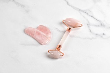 Pembe tekerlekli masaj aleti ve mermer arka planda guaj kazıyıcısı. Yaş karşıtı, cilt bakımı için spa ürünleri