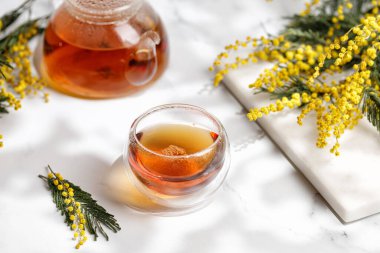 Duble Duvar Cam Bardağı ile çay ve mermer arka planda güneşli mimoza buketli cam çaydanlık.