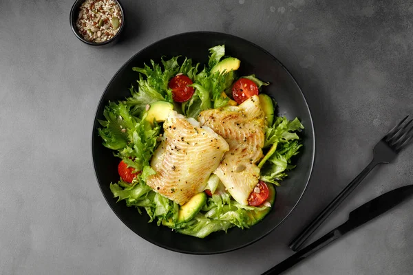 Sebze üzerine kızarmış halibut balığı ve taze yeşil salata. Üst Manzara. Siyah tabak. Çatal, bıçak.