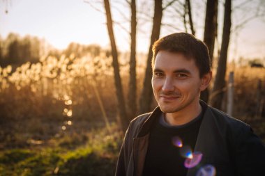 Neşeli yüzlü genç adam gün ışığında dışarıda yürüyor.