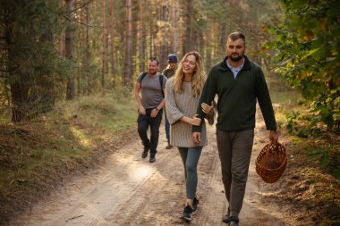 Güneşli ormanda yürüyen bir grup aktif arkadaşla flört eden genç bir çift.