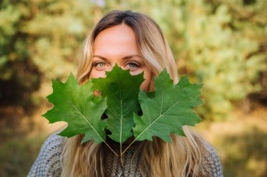 Genç çekici dışarıda yürüyor ve yüzünü meşe brunch 'ının arkasında üç yaprakla gizliyor.