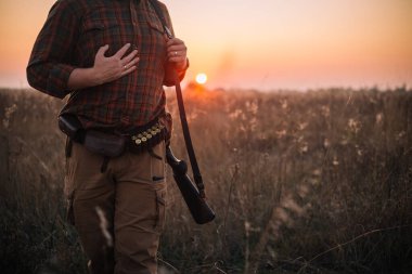 Tüfek ve cephane kemeri olan genç ve güçlü bir asker gün batımında toprak yoldan dışarı çıkıyor.
