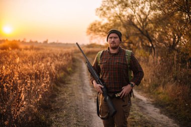 Tüfek ve cephane kemeri olan genç ve güçlü bir asker gün batımında toprak yoldan dışarı çıkıyor.