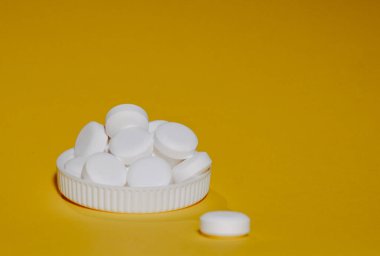 Beyaz başlıklı beyaz haplar sarı arka plan makrosu üzerinde