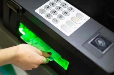 A female hand inserting a credit card into an ATM