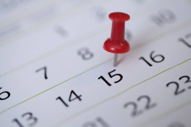 close-up of a person holding calendar with pin and a red marker with a marked day