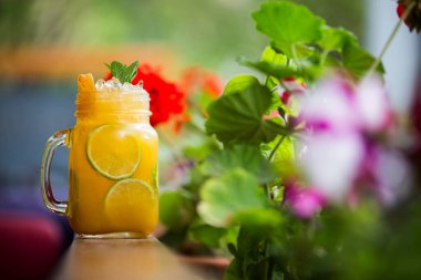 Ahşap bir yüzeyde, üzerinde güzel çiçekler olan bir kavanozda soğuk meyve çayı yakın plan çekimi.