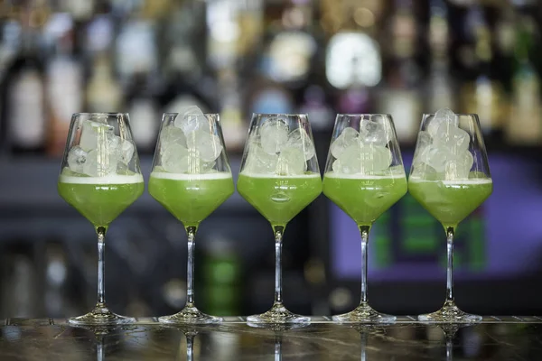Glass of green cocktail on bar background