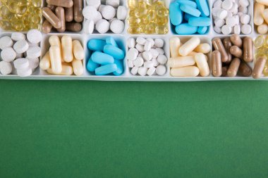 Yeşil arka planda hapları olan plastik bir kap.