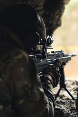 Makineli tüfek, yıkılmış bir binadaki fare deliğinden nişan alıyor. 