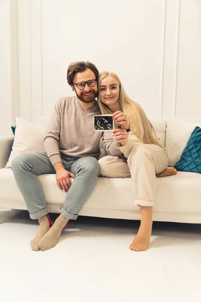 Foto vertical de extremamente feliz duas pessoas em um relacionamento segurando uma imagem de ultra-som de seu futuro bebê — Fotografia de Stock