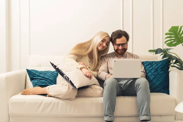 Белый бородатый мужчина с ноутбуком показывает что-то смешное на своей блондинке длинноволосой красивой женой — стоковое фото