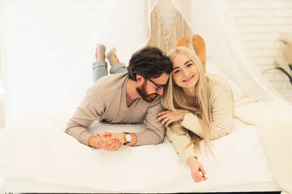 Morena alegre com sua adorável namorada de cabelos compridos deitada na cama, brincando e sorrindo — Fotografia de Stock