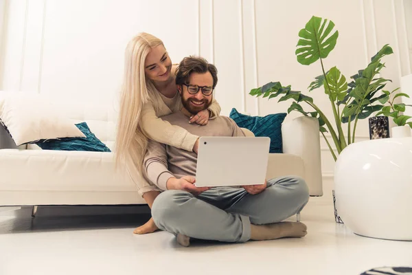 Aanhankelijk Kaukasisch paar zitten in de woonkamer en surfen op het internet met behulp van een zilveren laptop — Stockfoto