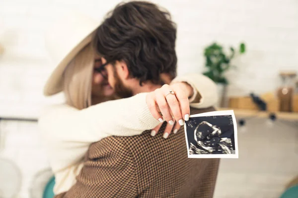 Bela mulher caucasiana surpreendendo seu namorado com uma imagem de ultra-som de seu futuro bebê — Fotografia de Stock