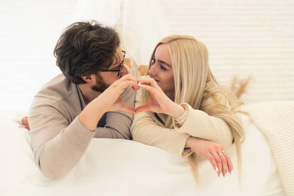 Lindo joven europeo casado pareja acostado en la cama y formando forma de corazón con sus manos, concepto de amor — Foto de Stock