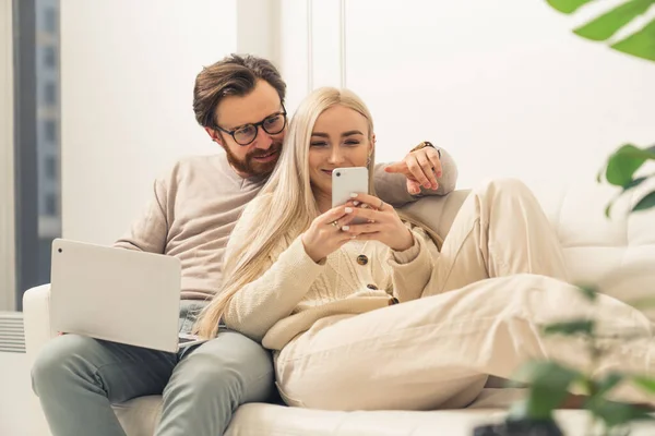 Moderne blanke jonge volwassenen zitten samen op een bank met een laptop en een telefoon, surfen op het internet — Stockfoto