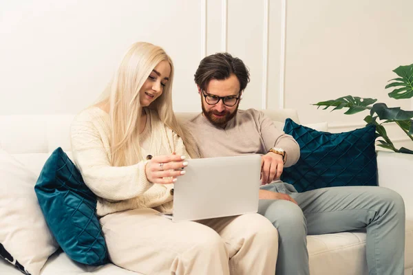 Happy woman browses laptop in nieuwe moderne flat, terwijl haar geïntrigeerd vriendje wijst naar het scherm. — Stockfoto