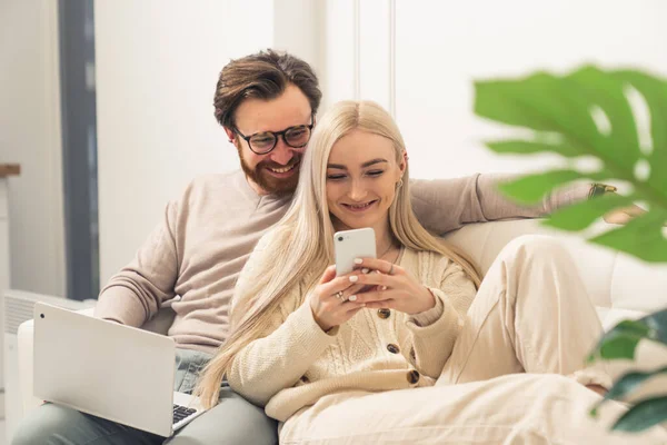 Portret van tevreden vrolijke duizendjarige paar lachen om een video gevonden op het internet en zitten op witte bank met laptop op de knieën — Stockfoto