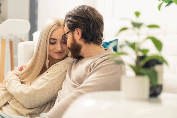 Aanhankelijke blanke jonge echtgenoten knuffelen en fluisteren terwijl ze op een bank zitten — Stockfoto