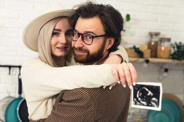 Futuros padres caucásicos abrazando y mostrando la imagen de ultrasonido de su bebé a la cámara —  Fotos de Stock