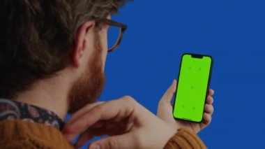 Kafkasyalı orta yaşlı işadamı, koyu mavi arka planda yeşil ekranlı akıllı telefon kullanıyor.