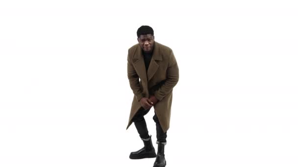 Afroamerican homme pliant et posant manteau brun fond blanc - plan complet. — Video