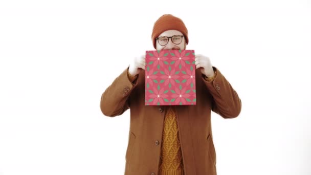 Hombre hipster de mediana edad revelando su cara sonriente feliz detrás de una colorida bolsa de papel blanco fondo estudio disparo — Vídeo de stock